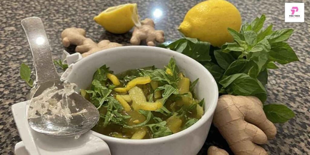 A bowl of green mango chutney garnished with herbs sits on a speckled countertop, surrounded by fresh ginger, lemons, and basil leaves, conveying a fresh, zesty tone.